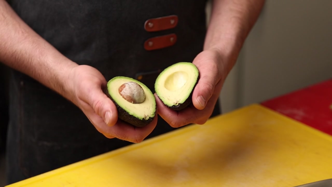 Nærbillede af hænder, der åbner en frisk moden avocado