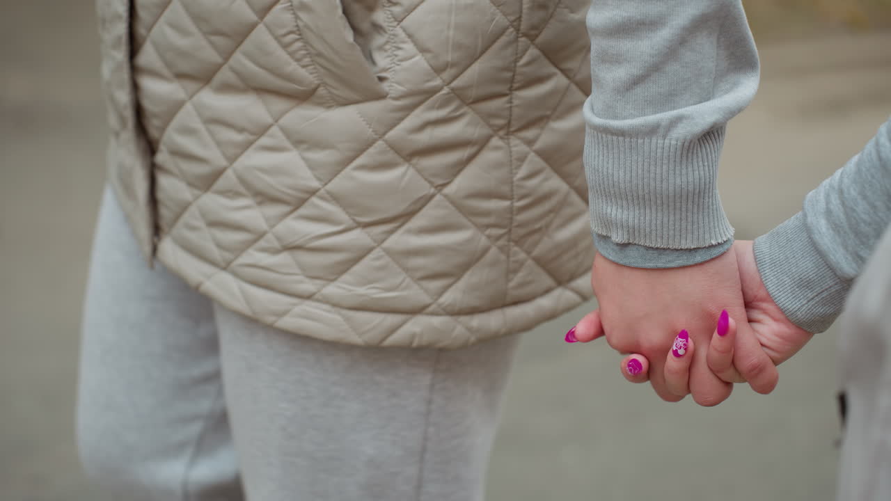 Couple walking hand in hand with woman purple polished nails visible, fingers gently intertwined while strolling on tarred road, wearing casual cozy outfits, blurred background
