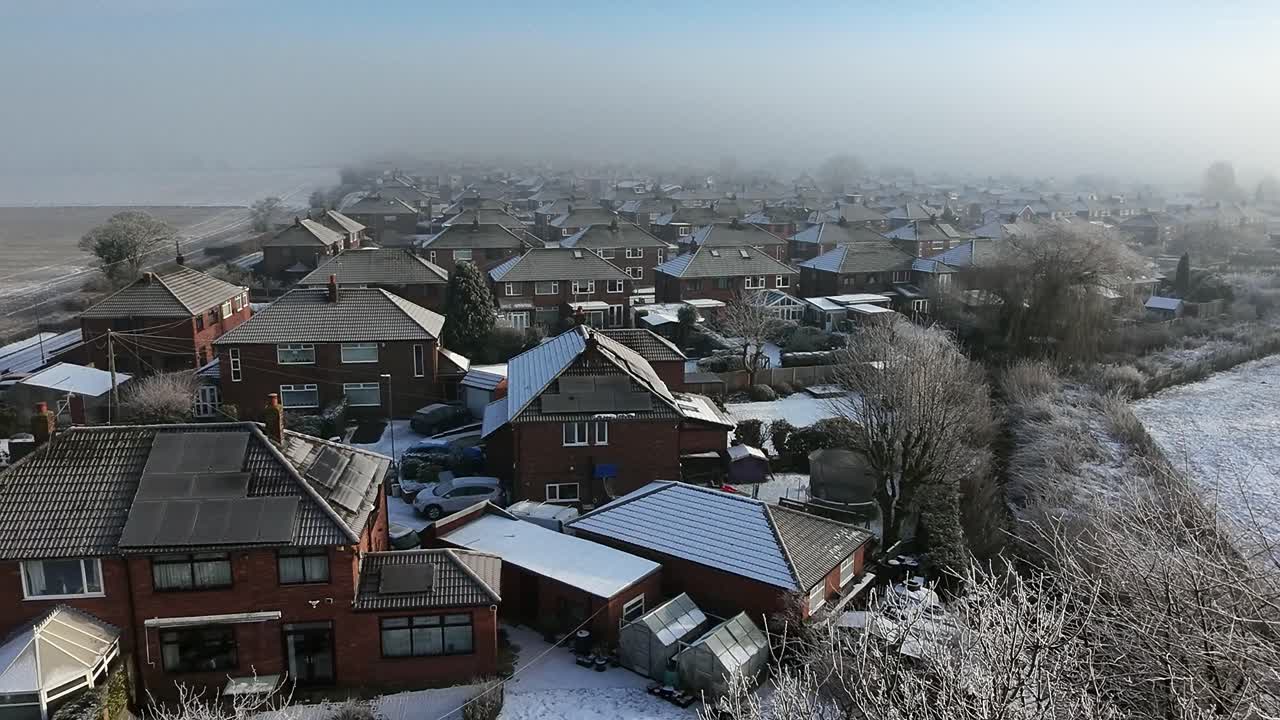 Frosty morning mist aerial view covering small town houses and agricultural field in England