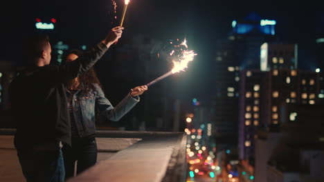 Glückliches-Kaukasisches-Paar,-Das-Sich-Nachts-Auf-Dem-Dach-Küsst-Und-Wunderkerzen-In-Der-Hand-Hält,-Jubiläum-Feiert-Und-Den-Romantischen-Silvesterabend-In-Der-Stadt-Genießt