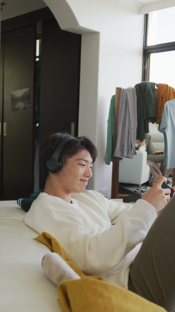 아시안 남성 십대가 거실에서 비디오 게임을 하는 수직 비디오