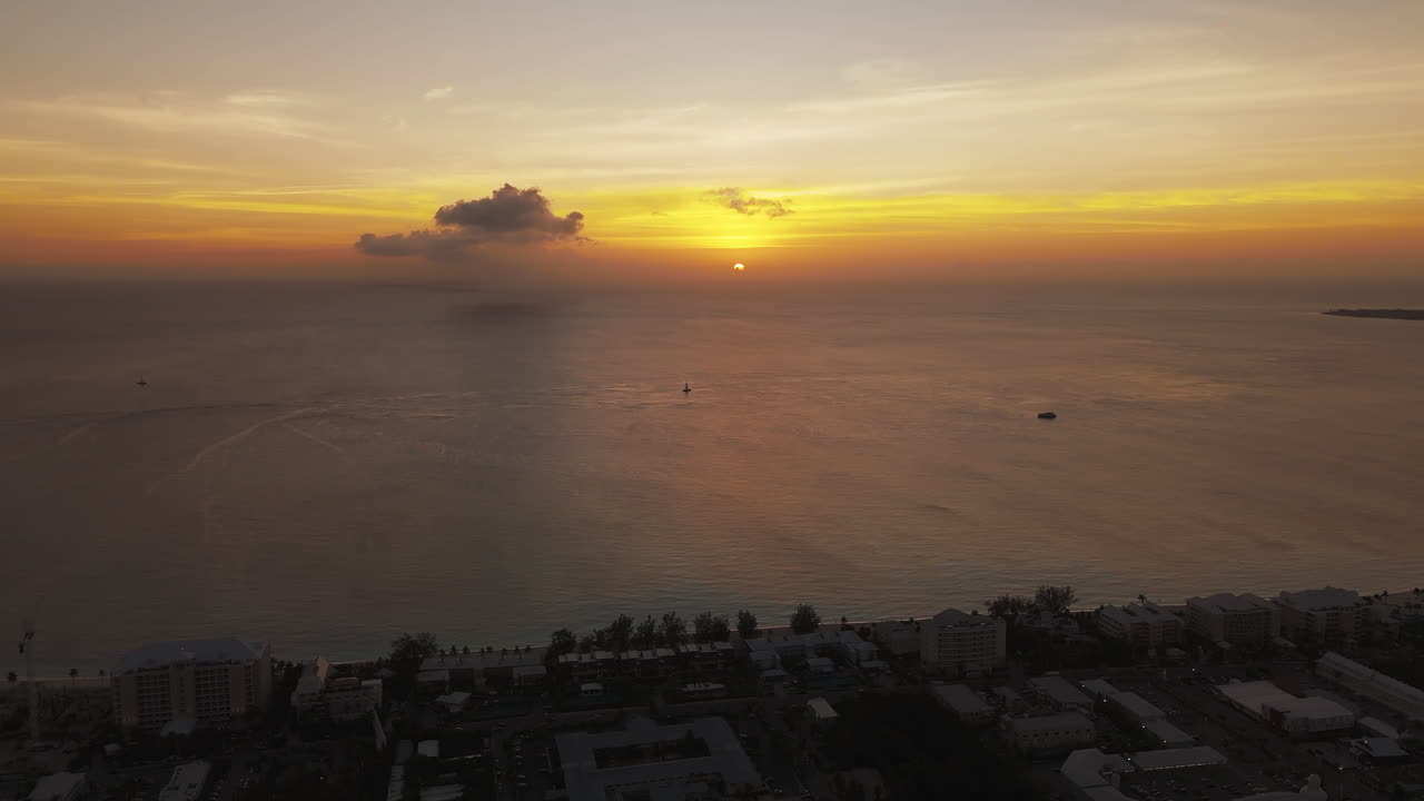 Aerial descend over Seven Mile Beach at sunrise, glowing Caribbean waters of Grand Cayman