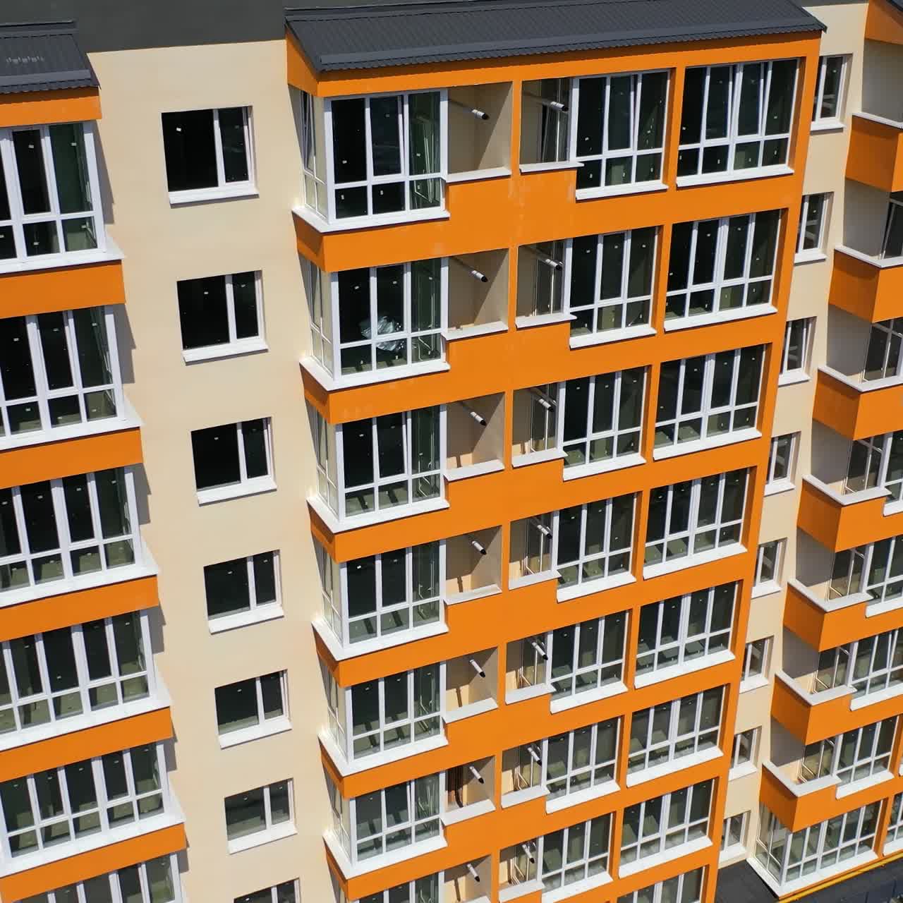 New high-rise building of modern design. Multi storey building with large covered balconies in orange color. Motion camera down