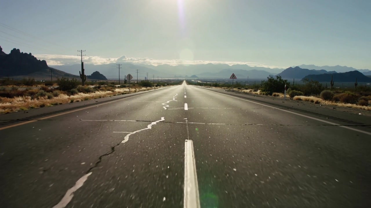 Starting low center camera moving forward to reveal mountains on desert road, with white centerline