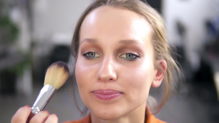 Front view of a beautiful smiling female model during the make up process. Make up artist completes the work, putting some