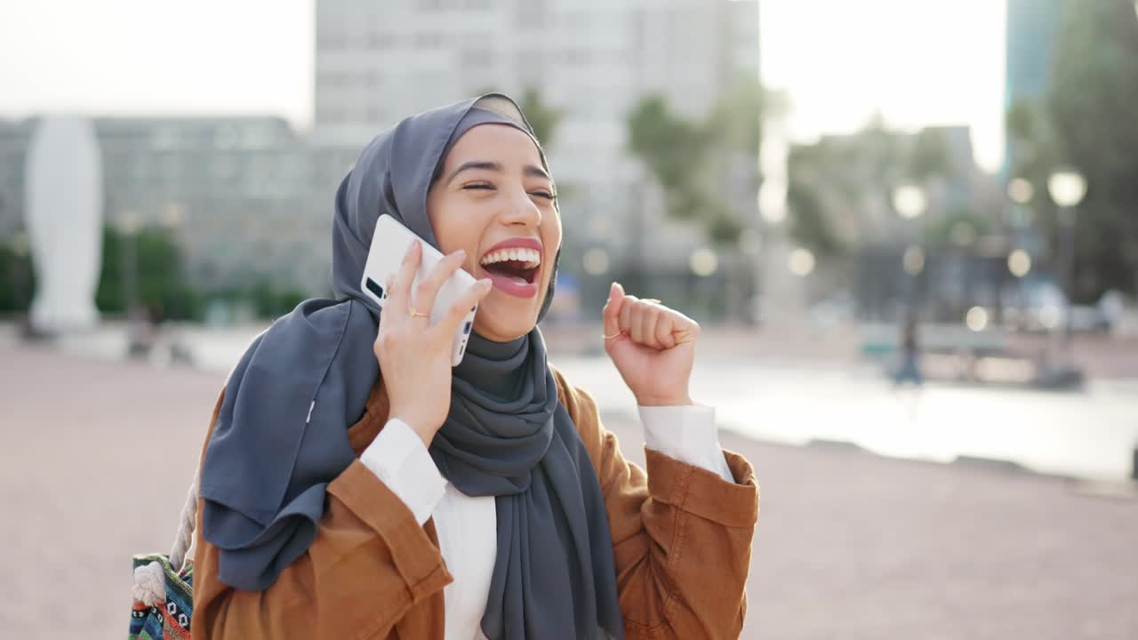Excited woman in hijab celebrates good news on a phone call in an urban setting