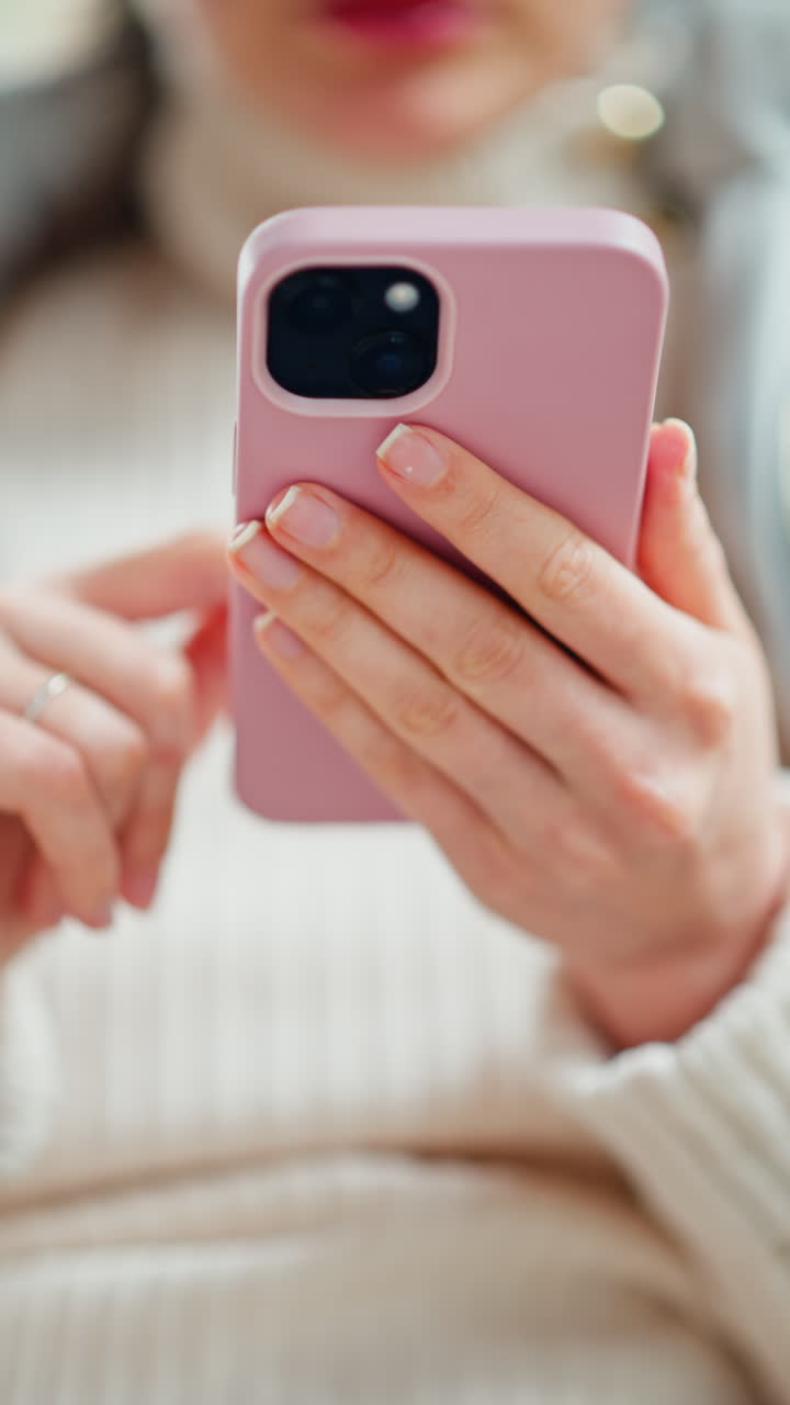 Woman in jacket scrolling through her phone at a cafe. Vertical