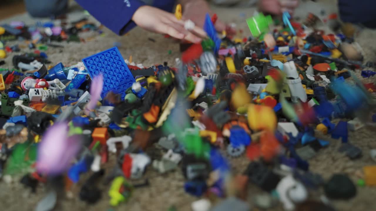 Unrecognizable hands throwing many lego blocks on the floor in the room. A lot of small colorful lego bricks in a mess lying on the carpet.
