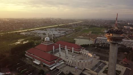 circle drone shot of the great mosque of central java (majt) in suset time. th sun is orange and the weather is cloudy. it have some pillars and some umbrela that is closed and a big tower