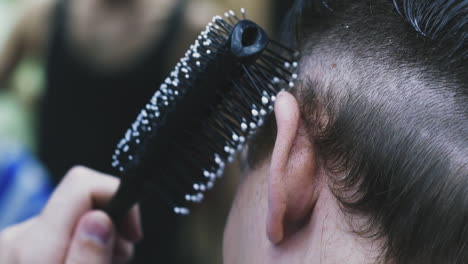 el peluquero hace el corte de pelo al cliente cepillando el cabello en las sienes