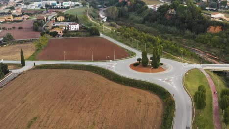 Aerial-view-of-a-runner-passing-through-a-roundabout-in-a-town-surrounded-by-nature-during-the-day