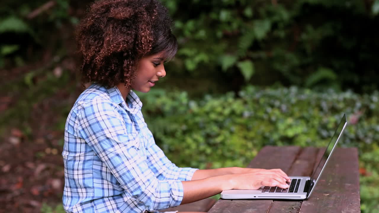 Gorgeous content brunette sitting at picnic table using laptop