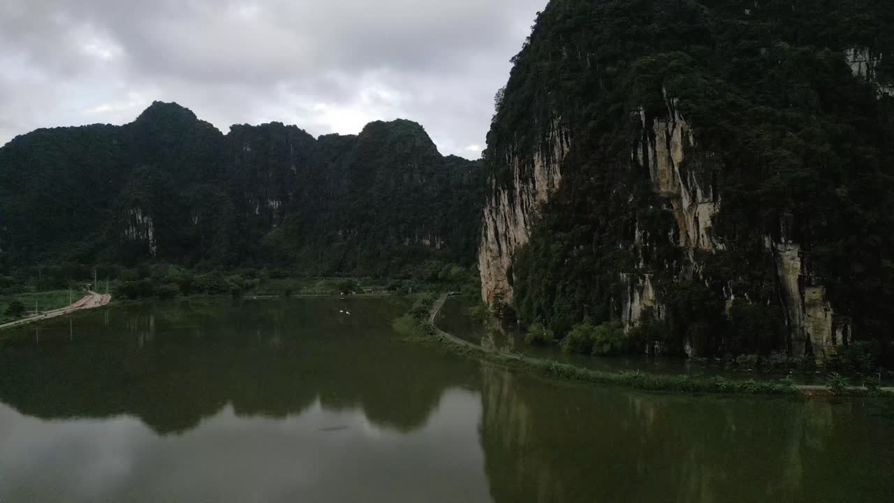 Aerial shot of a bird flying above a still lake in the green lush asian mountains