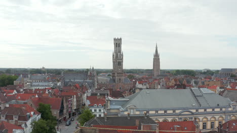 Glockenturm-Von-Brügge-Glockenturm-Aus-Der-Luftdrohnenperspektive-Und-Taubenvögel,-Die-Mit-Bewölktem-Himmel-Fliegen