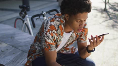 African-american-man-in-city,-sitting-on-step-drinking-coffee-and-using-smartphone-in-the-street