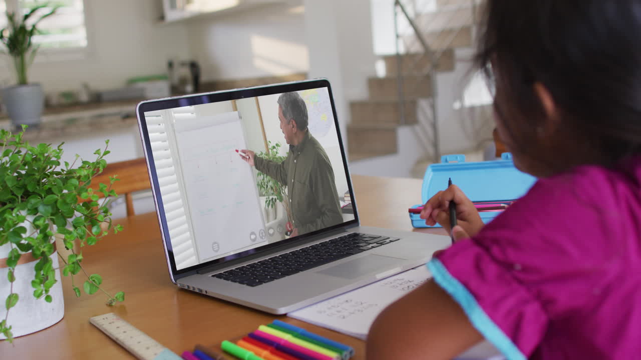 chica biracial sentada en un escritorio usando una computadora portátil teniendo una lección escolar en línea