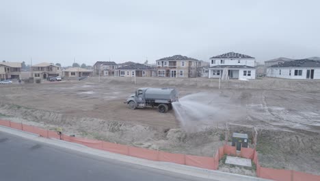 a drone observes a water truck as it diligently dumps water on a dirt lot within a home construction site, facilitating the site's preparation