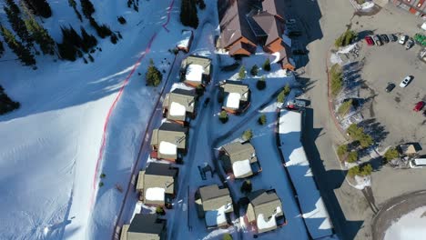 drone glides above snowy mountain condos arranged along winding roads, with snow-draped trees and distant peaks in view, capturing a tranquil vacation rental scene in winter