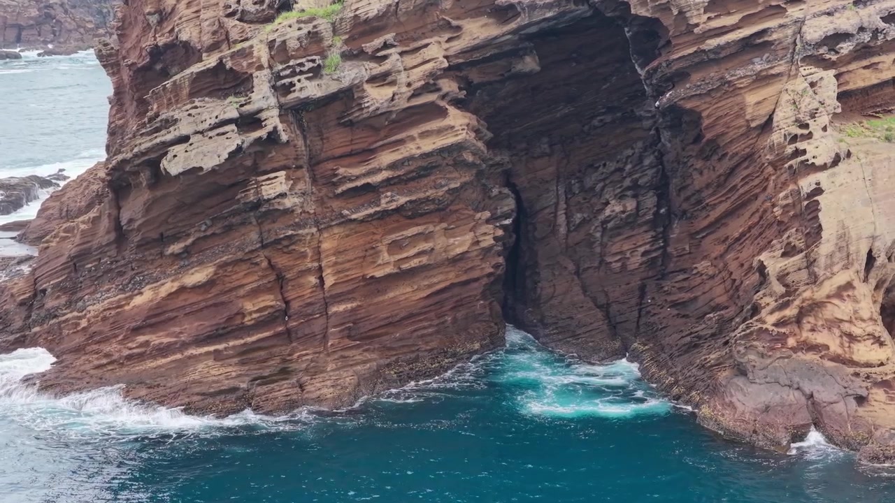 Horizontal aerial close view near Eongal Coastal Trail and Chagwido on Jeju Island, South Korea, showing layered volcanic cliffs and a sea cave as the camera trucks left while facing right