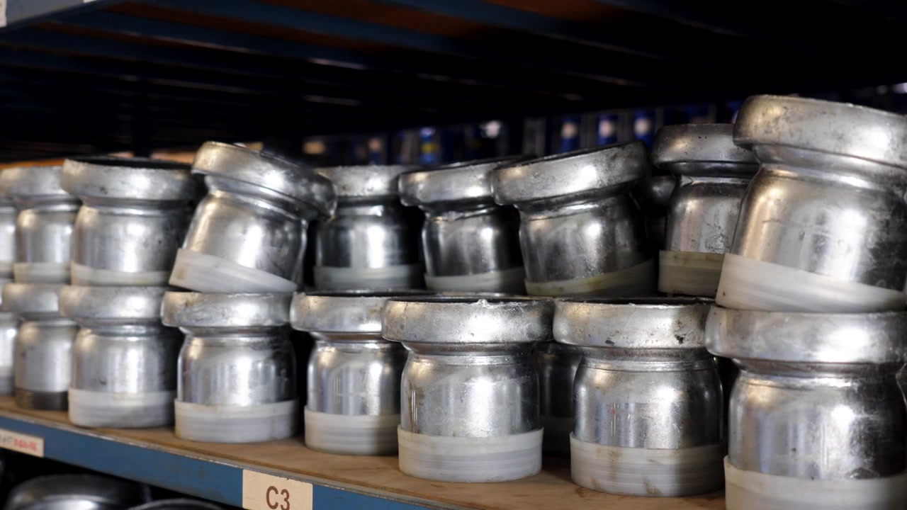 Acoplamientos de tuberías metálicas apilados en estantería de almacén para sistemas de riego industrial, primer plano medio