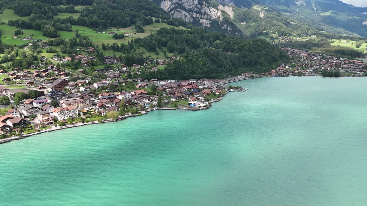 曇天の穏やかな日差しのもと、スイス、ベルナーオーバーラント地方の息をのむようなターコイズブルーのブリエンツ湖沿いにある魅力的なアルプスの村ブリエンツへ、ドローンが降下していく。