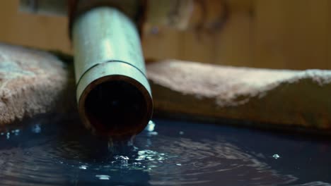 el agua termal natural fluye de la tubería de bambú al baño de piedra en onsen