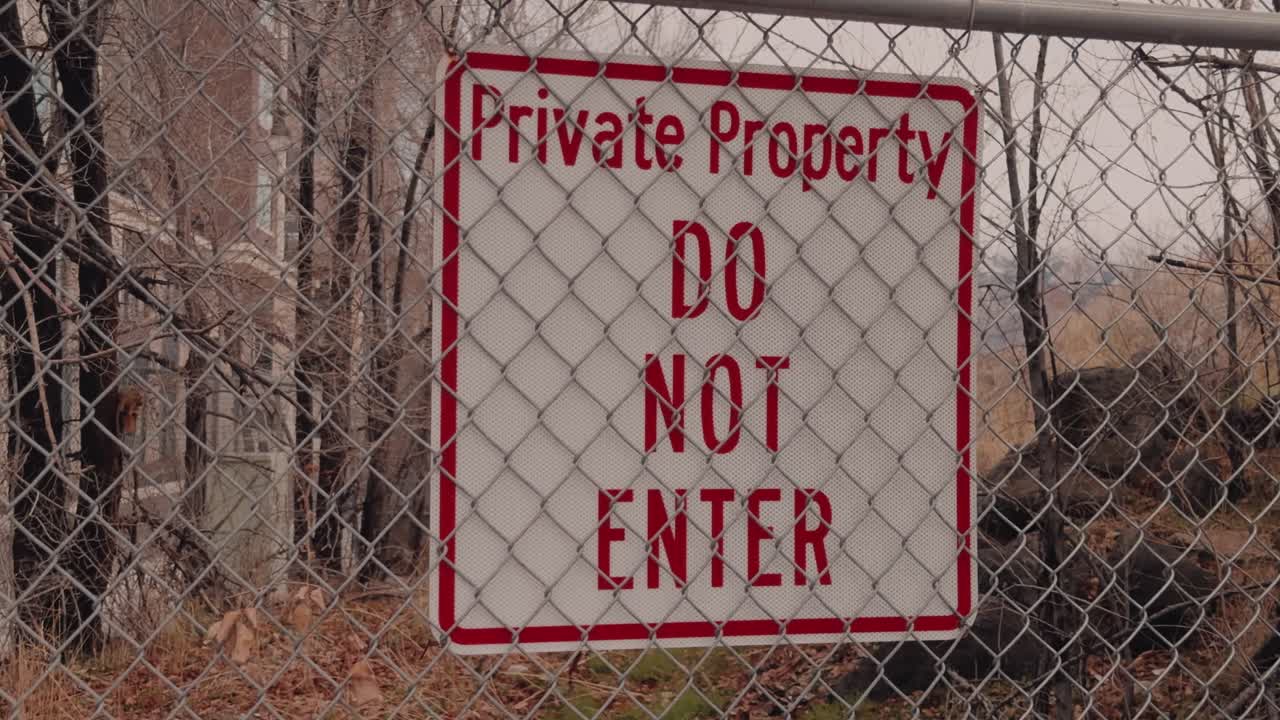 Slow zoom toward private property warning sign behind a chain link fence in winter