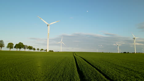 Slow-aerial-flyover-green-farm-field-towards-wind-turbine-farm-in-the-evening