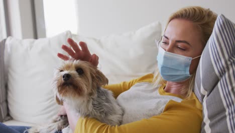 mujer con máscara facial sosteniendo a su perro mascota en casa