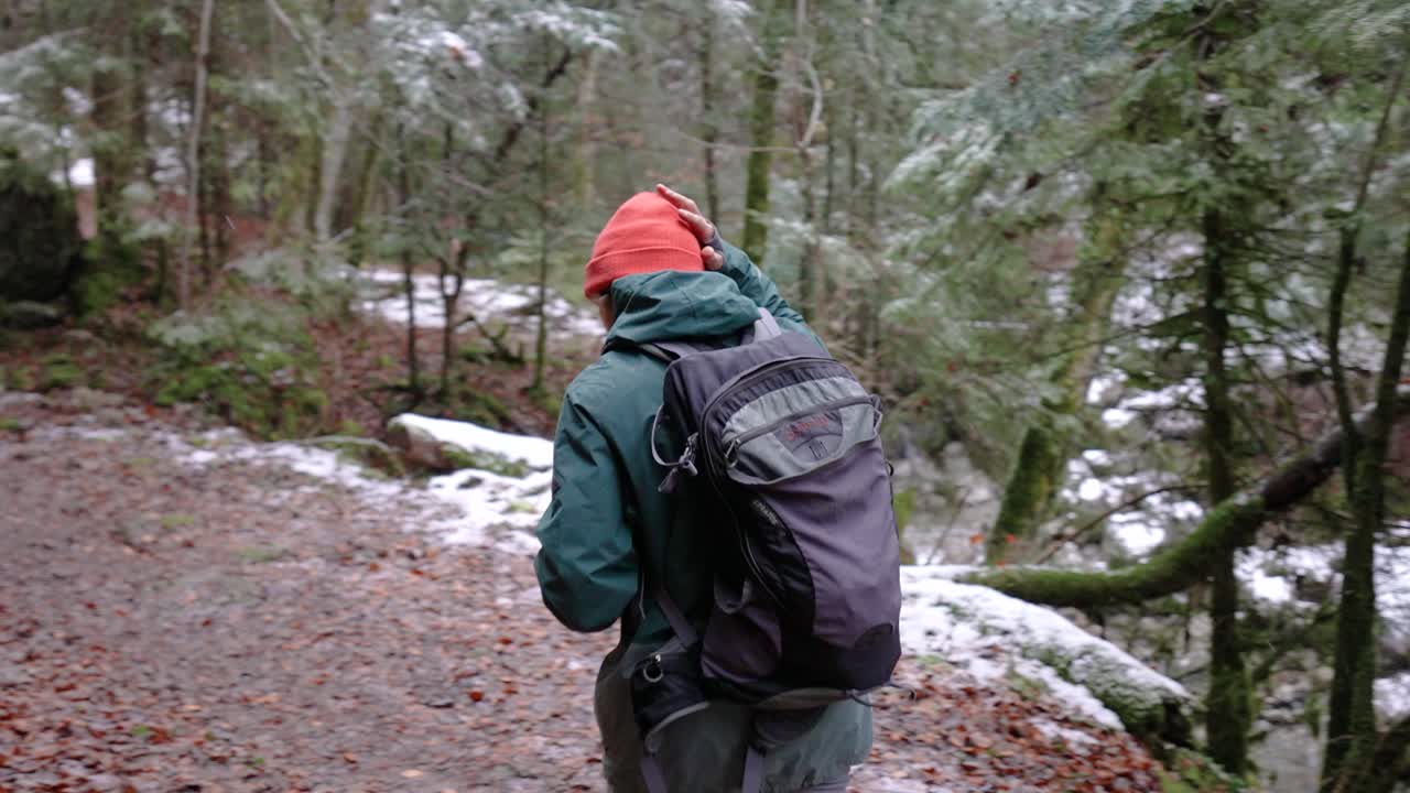 Photographer With Backpack And Camera Walking Deep In Forest During Snowfall In Winter. - reveal, tracking shot