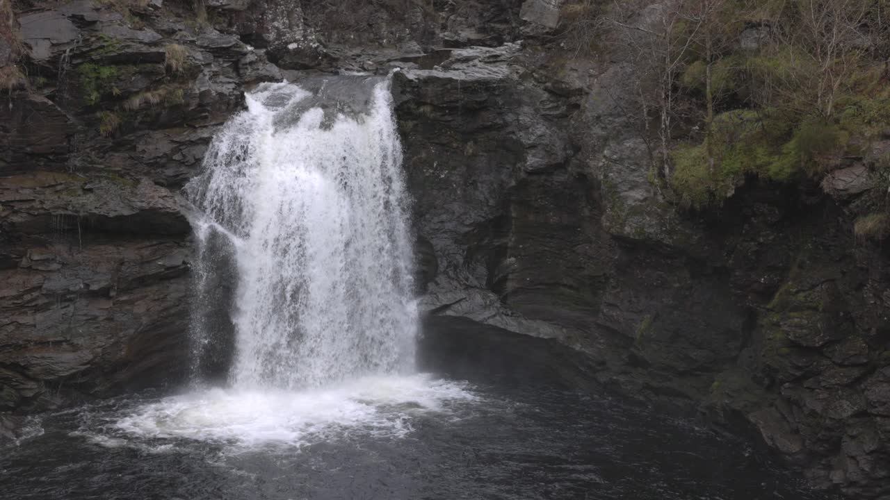 Slow motion high shot of water flowing over the Falls of Falloch in Scotland