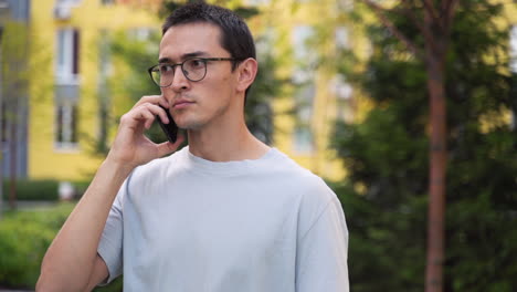 屋外の通りに立ちながら携帯電話で話している深刻な若い日本人男性