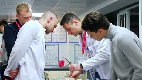 group of men standing around the table. pedagogue wearing white robe demonstrates usage of neurosurgical tools at spine dummy.
