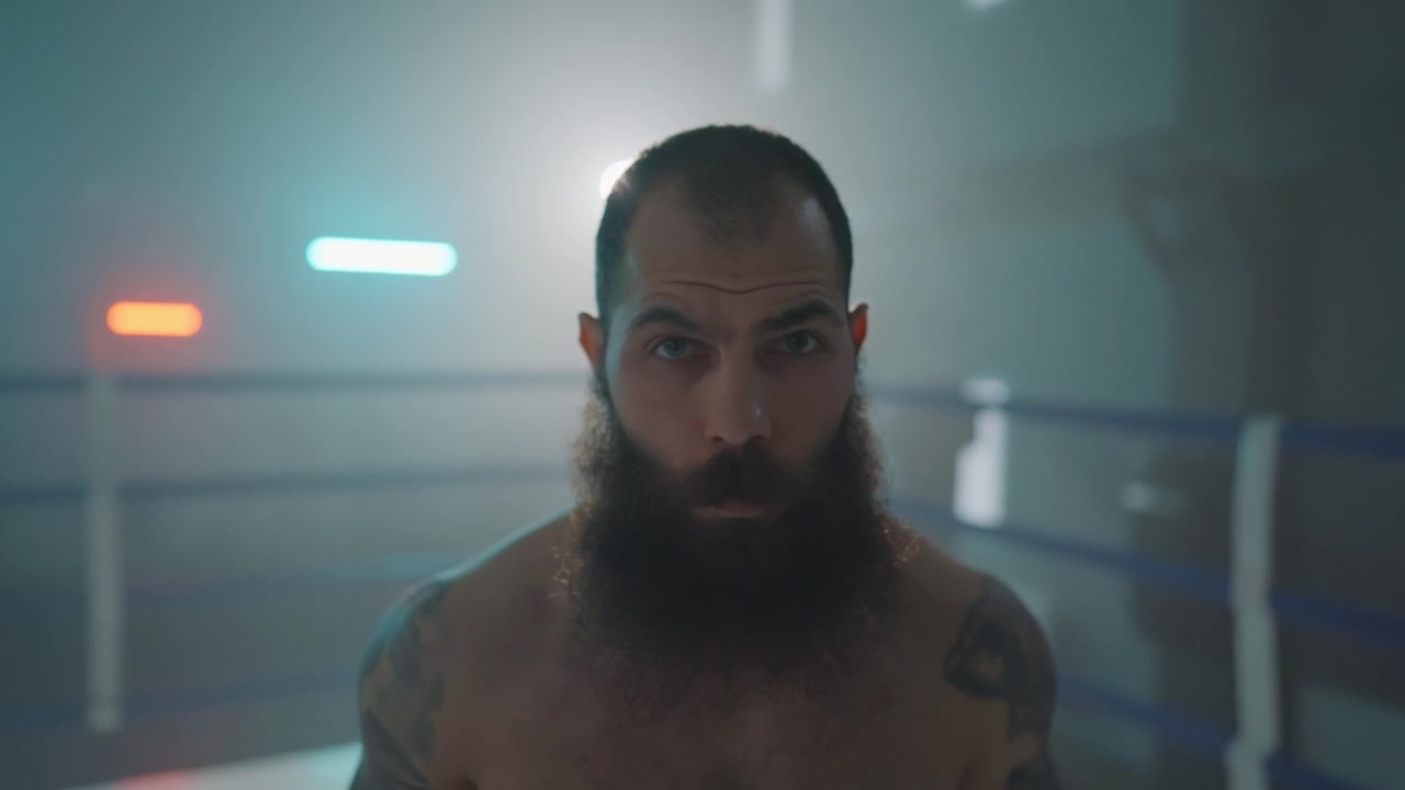 Primo piano di un serio combattente barbuto su un ring di pugilato.