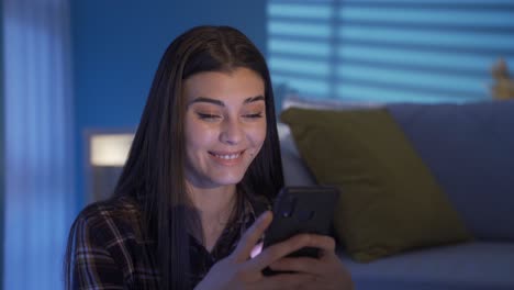 happy young woman sitting on the floor by the sofa looking at the phone with a smile. texting.