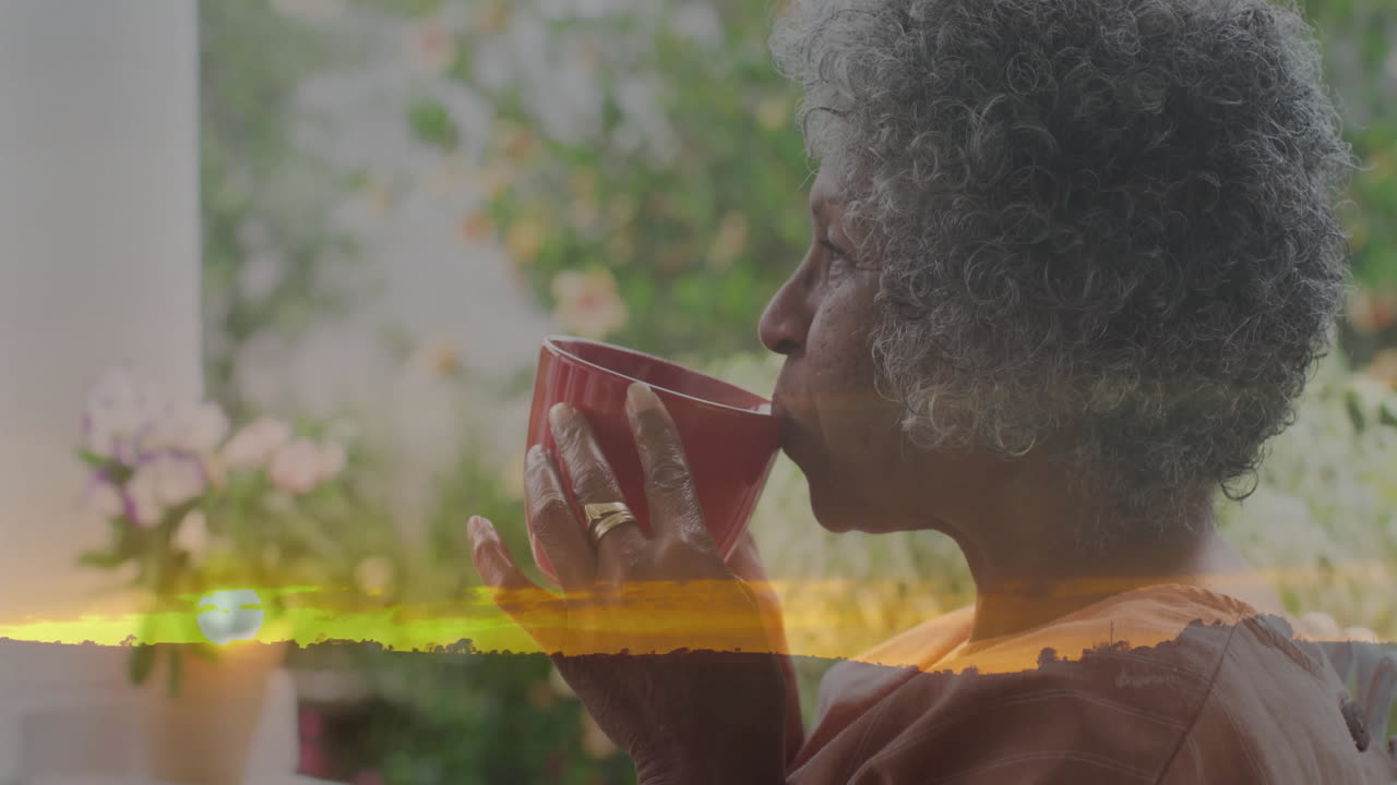 Drinking from red cup, elderly woman enjoying animation of sunset landscape