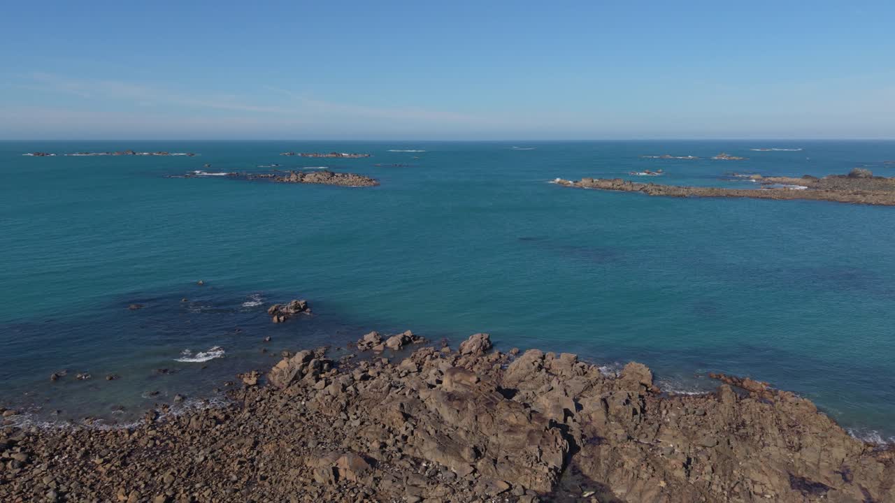 Scorcio ravvicinato di costa rocciosa e mare azzurro e limpido sotto il sole del tardo pomeriggio, con vista sul mare calmo e affioramenti rocciosi fino all'orizzonte.