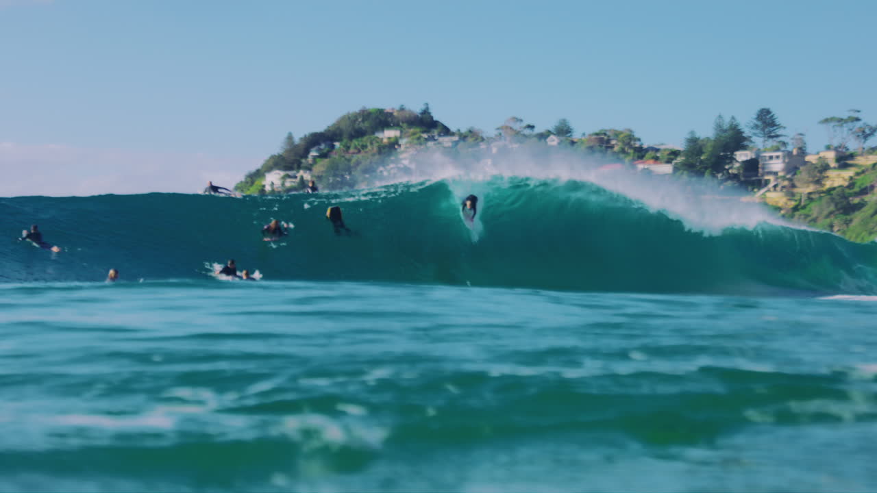 Slow motion view of surfers in water at surface of ocan as they kick and paddle to drop into barreling wave
