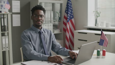 portrait of visa officer sitting at desk with laptop in american embassy