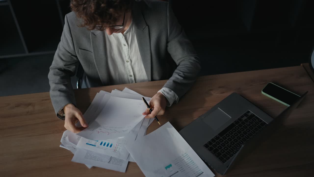 primer plano de un joven confiado en un traje gris examinando documentos e informes de trabajo sentado en una mesa en la oficina