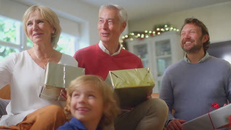 multi-generation family exchanging and opening gifts around christmas tree at home