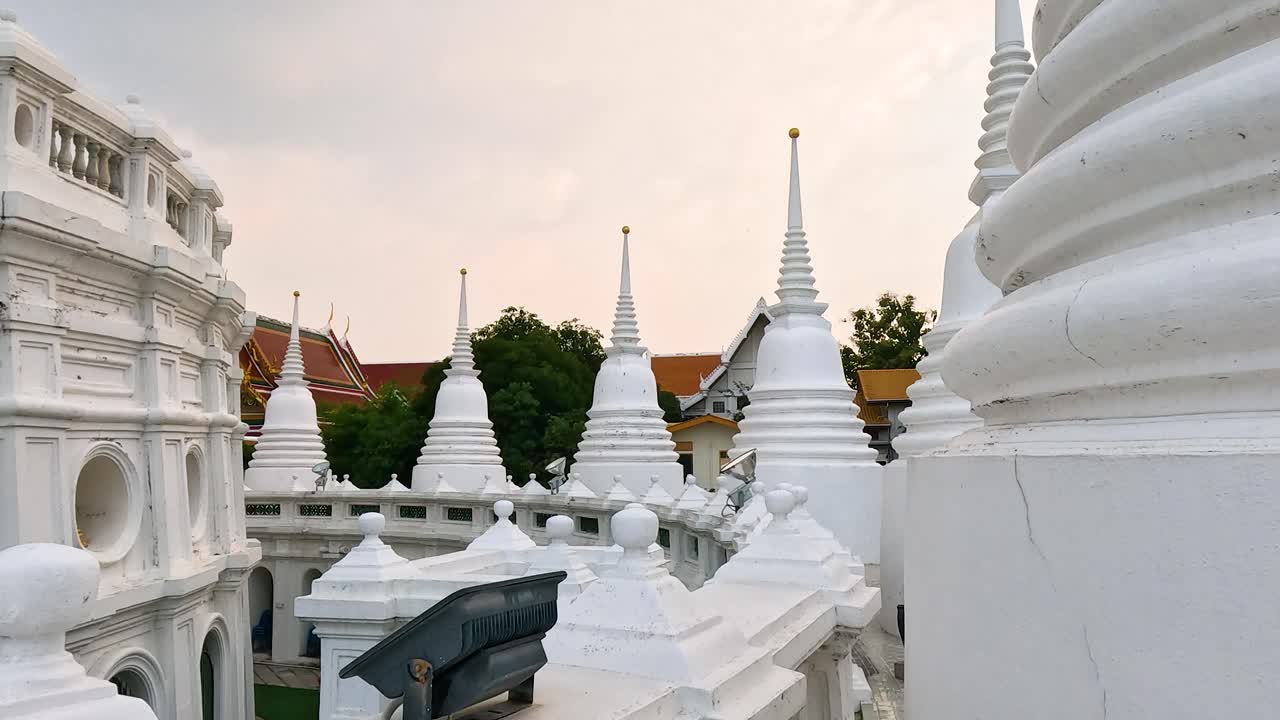 Stupa bianchi e architettura ornata sotto una luce diurna soffusa a Wat Prayurawongsawas, Bangkok, che mettono in mostra il design tradizionale dei templi thailandesi.