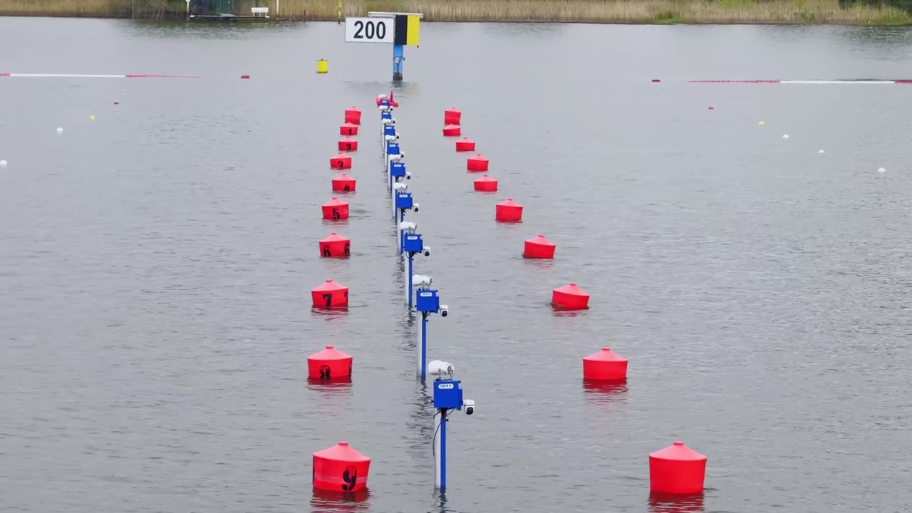Canoe sprint course lane markers on a Brandenburg lake, with red buoys, blue timing equipment, 200 meter sign and calm grey race water.