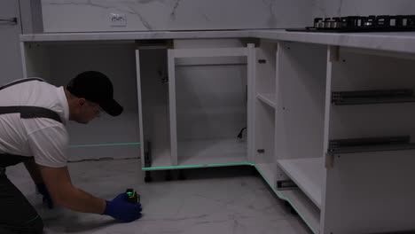 a qualified craftsman in gray overalls installs furniture using a construction laser