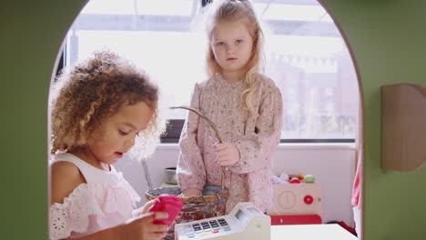 three kindergarten schoolgirls playing shop in a playhouse at an infant school, backlit