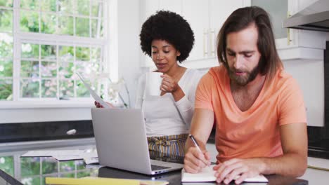 Glückliches-Gemischtrassiges-Paar,-Das-Laptop-Benutzt-Und-In-Der-Heimischen-Küche-Finanzen-Berechnet