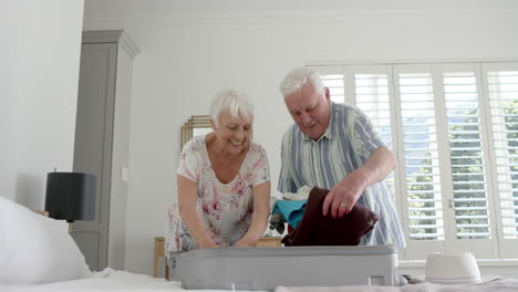 Senior-caucasian-couple-packing-suitcase-in-bedroom-at-home,-slow-motion