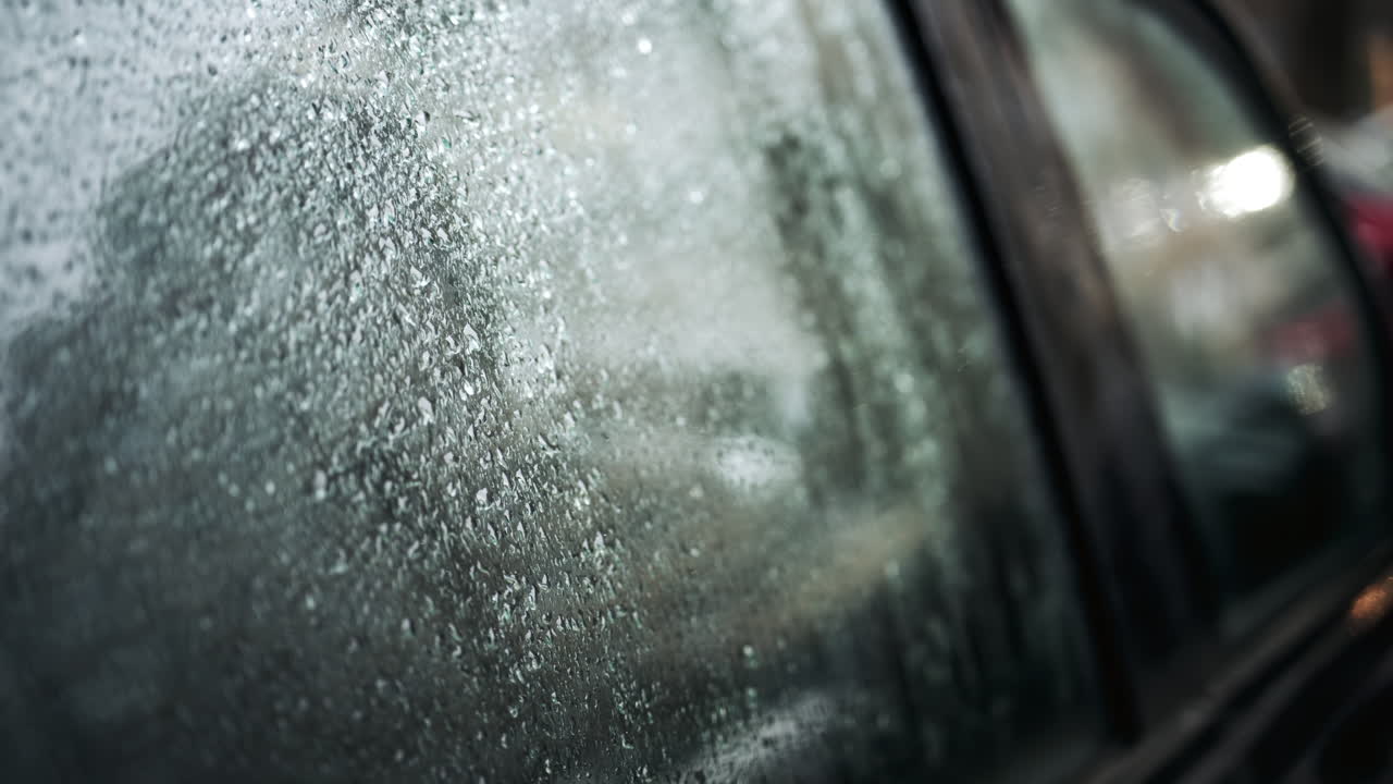 Close up of raindrops covering car window glass with blurred urban background
