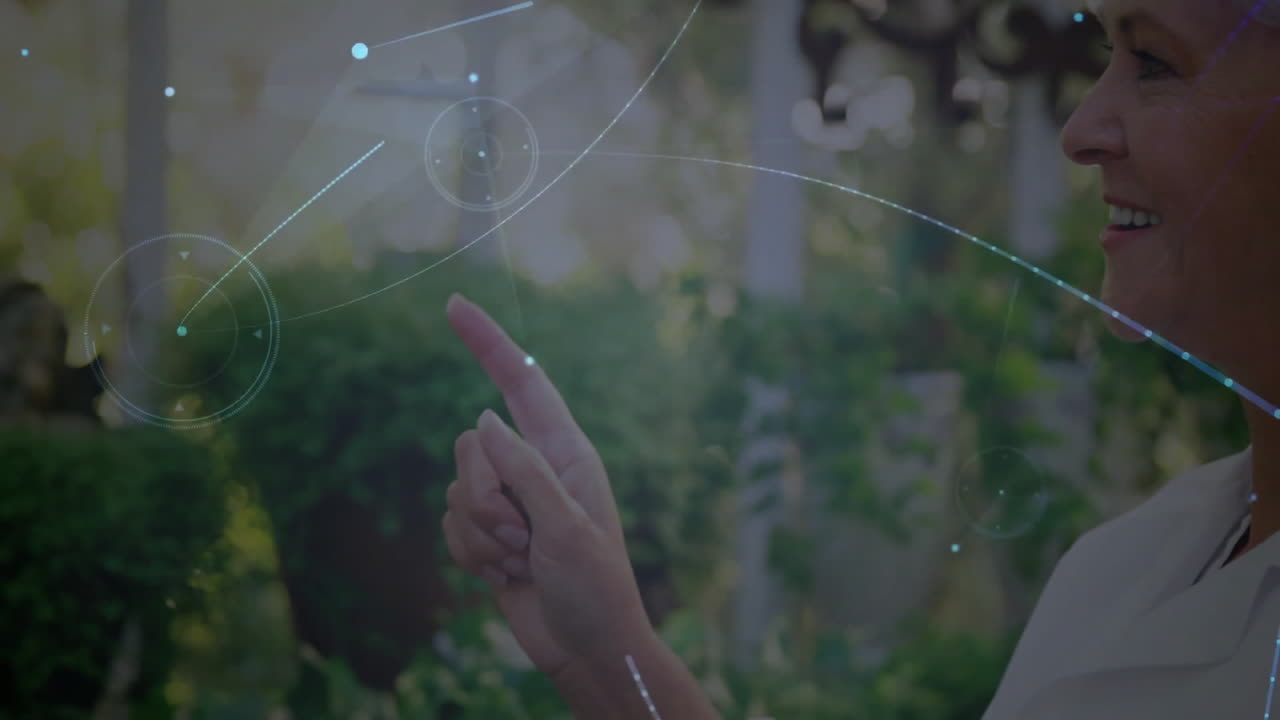 Senior woman pointing holographic circular HUD interface in garden, showing tech interface design