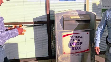 un hombre latino vota en las elecciones dejando caer una carta de votación por correo en la ranura de la cabina de votación con el cartel oficial de votación para la campaña del gobierno democrático en la carrera presidencial